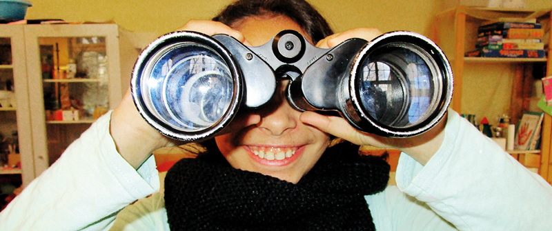 Schulbezogene Sozialarbeit an der Ludwig-Cauer-Grundschule, Berlin Charlottenburg, Mädchen blickt durch ein Fernglas